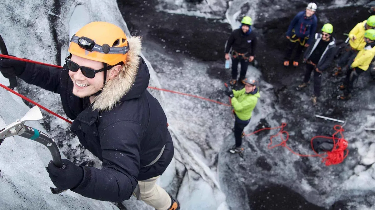 Climber on a vertical blue ice wall with axes during the ice climbing add-on to a Sólheimajökull glacier hike, Iceland